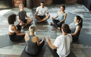 Seven yogis sitting in a circle on yoga mats, meditating