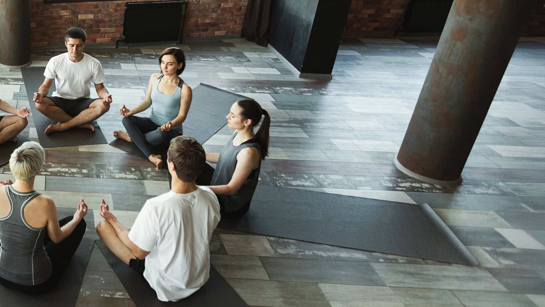 A group of 7 yogis sitting on yoga mats on the floor in a circle with meditative intention